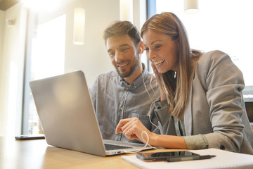 Work colleagues sharing headphones looking at computer
