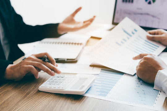 Two young colleagues using calculator together and analysis summary report graph in a modern office.
