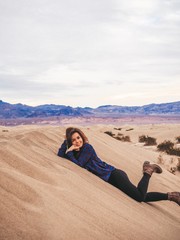 Fototapeta na wymiar Girl with long hair in a plaid shirt sitting on a sand dune in Death Valley