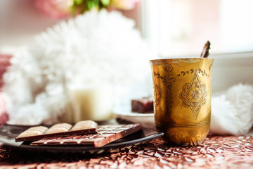Black plate with chocolate bar an antique silver cup. White blurred background.