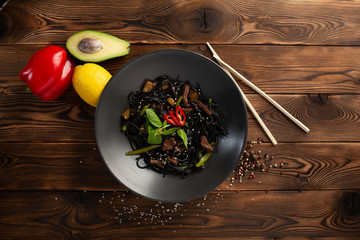 black noodle with marbled beef in a black plate on a wooden background
