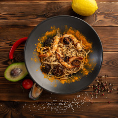Singapore-style noodles with shiitake mushrooms and shrimps in a black plate on a wooden background