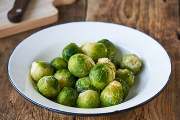 Frozen brussels sprouts in a white bowl on a wooden background