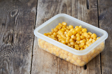 Canned corn in a plastic container on a wooden background