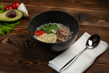 Japanese pho bo soup in a black plate on wooden background