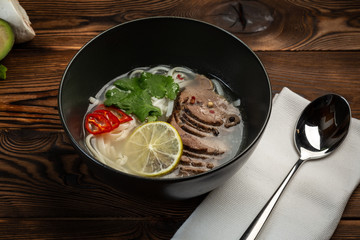 Japanese pho bo soup in a black plate on wooden background