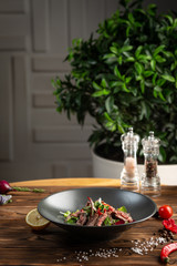 Thai beef salad in black plate on wooden background
