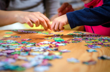 Hands of a little child and parent playing jigsaw puzzle game on a  table