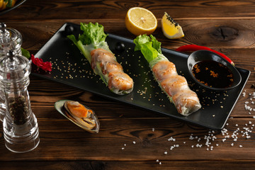 Asian spring rolls with shrimp in a black rectangular plate on a wooden background