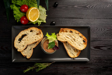 Japanese duck pate with warm ciabatta on a black plate on a black wooden background