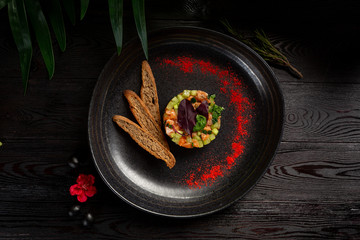 salmon tar-tar on a black plate on a wooden background