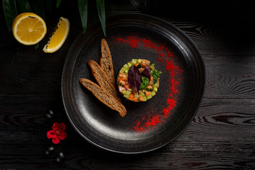 salmon tar-tar on a black plate on a wooden background