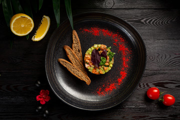 salmon tar-tar on a black plate on a wooden background