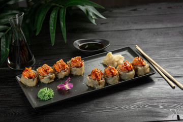 set of sushi rolls on a black rectangular plate on a black wooden background
