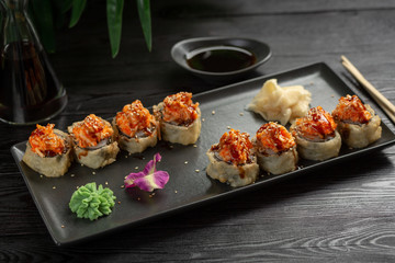 set of sushi rolls on a black rectangular plate on a black wooden background