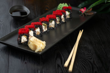 set of black sushi rolls on a black rectangular plate on a black wooden background