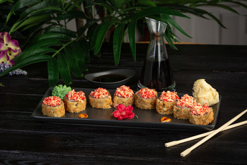 set of sushi rolls on a black rectangular plate on a black wooden background