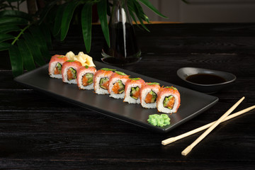 set of sushi rolls on a black rectangular plate on a black wooden background