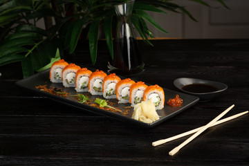 set of sushi rolls on a black rectangular plate on a black wooden background