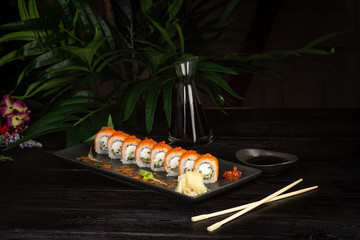 set of sushi rolls on a black rectangular plate on a black wooden background