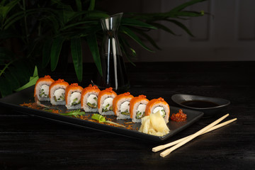 set of sushi rolls on a black rectangular plate on a black wooden background
