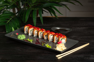set of sushi rolls on a black rectangular plate on a black wooden background