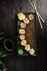 set of sushi rolls on a black rectangular plate on a black wooden background