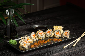 set of sushi rolls on a black rectangular plate on a black wooden background