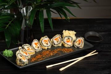 set of sushi rolls on a black rectangular plate on a black wooden background