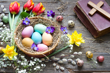 Easter colorful eggs in the nest with flowers on vintage wooden boards with bible and cross