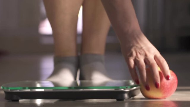 The woman measuring the weight by means of scales. Nearby apple lies. Weight became less.