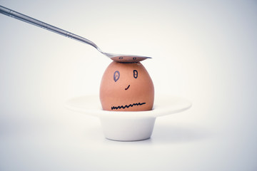 Spoon breaks sad egg on a stand in the form of human head . Concept.