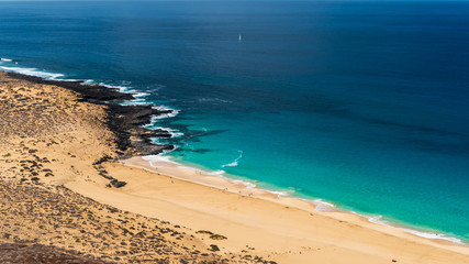 Exotic Las Conchas beach seen from above, a tropical paradise on La Graciosa Island, Canary, with turquoise sea waters in infinite shades of blue contrasting the white sand and volcanic black rocks.