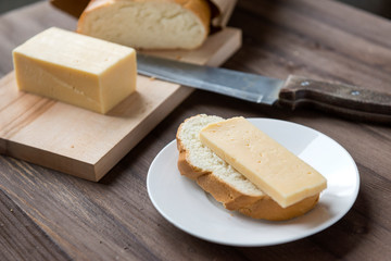 piece of cheese on bread on a white plate, loaf, knife, wooden background, sandwich