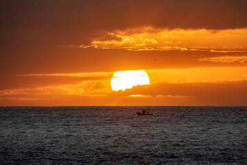 Sunset over the ocean with small fishing boat