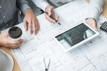 Construction engineering or architect discussing a blueprint and building model while checking information on sketching meeting for architectural project in work site