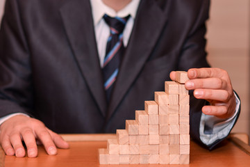 The last step in the business. Businessman's hand puts the last wooden block on the ladder