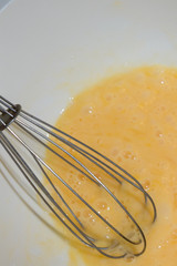 Whipping chicken eggs with a metal whisk in a mixing bowl