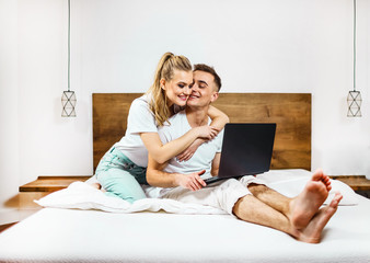 Young blonde couple browsing internet at home,using laptop and smiling