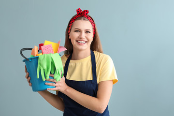 Portrait of beautiful woman with cleaning supplies on color background