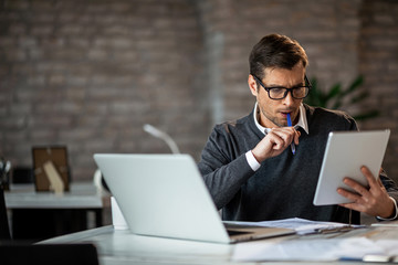Mid adult businessman using digital tablet while working at his desk in the office.