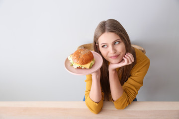 Young woman with tasty burger at table