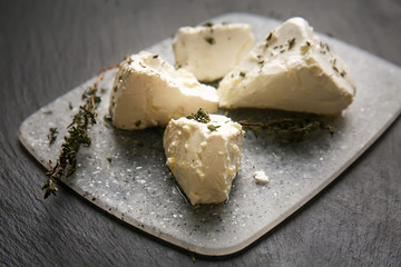 Board with tasty feta cheese and thyme on dark table
