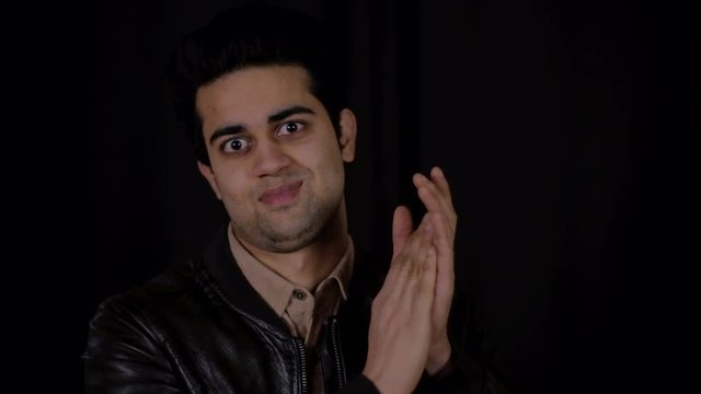 Young Indian man smug and confident looks at the camera with sarcasm and does a condescending slow clap of mock approval 