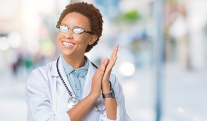 Young african american doctor woman wearing medical coat over isolated background Clapping and...