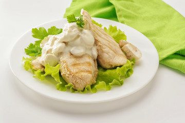 Fried chicken breast with cream sauce and mushrooms on a white plate and a green napkin. White background