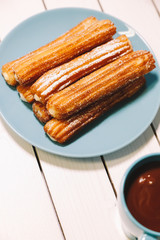 spanish fritters and hot chocolate served on blue dish and cup on a wooden table