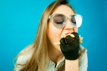 girl eating French fries on blue background, beautiful young blonde girl with long hair eating fast...