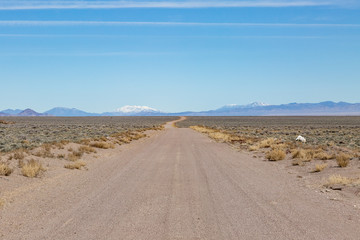 Fototapeta na wymiar A long dusty road in the Nevada desert, with a snowcapped mountain in the distance