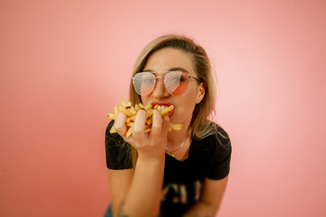 young beautiful blonde girl model with appetite eating fast food, French fries holding in hand, on...